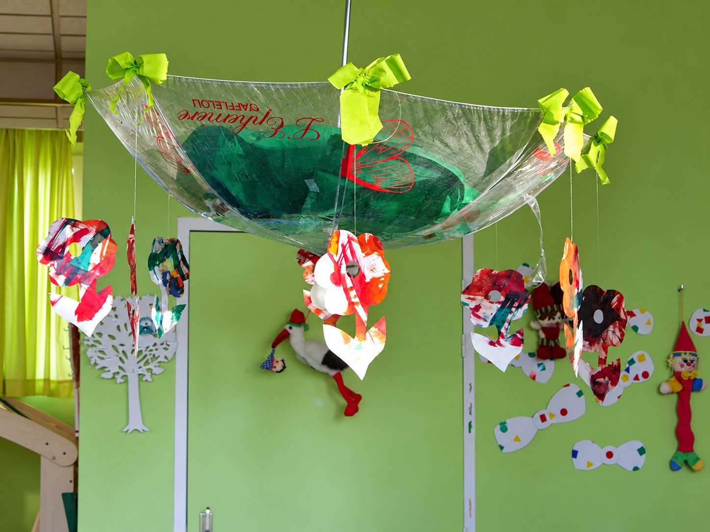 Un parapluie transparent retourné, décoré de rubans verts et de fleurs en papier peint, suspendu dans une salle de jeux