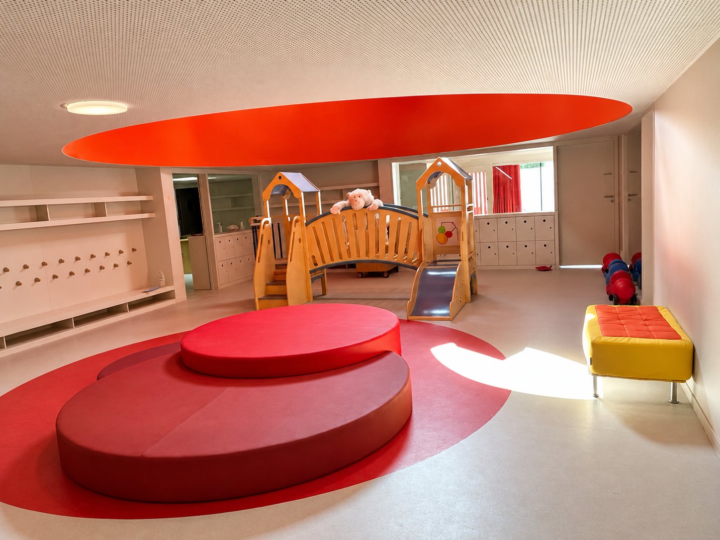 Le hall de La Grande Ourse : grands coussins ronds rouges, petit pont en bois et banc jaune sous un plafond rouge